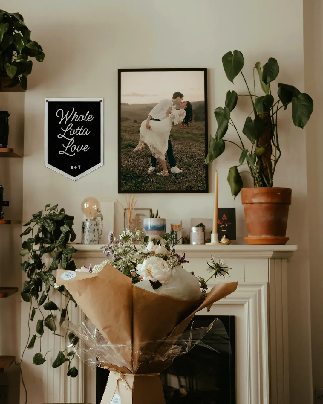 Decorative setting with a bouquet, framed photo, and plants on a mantelpiece.