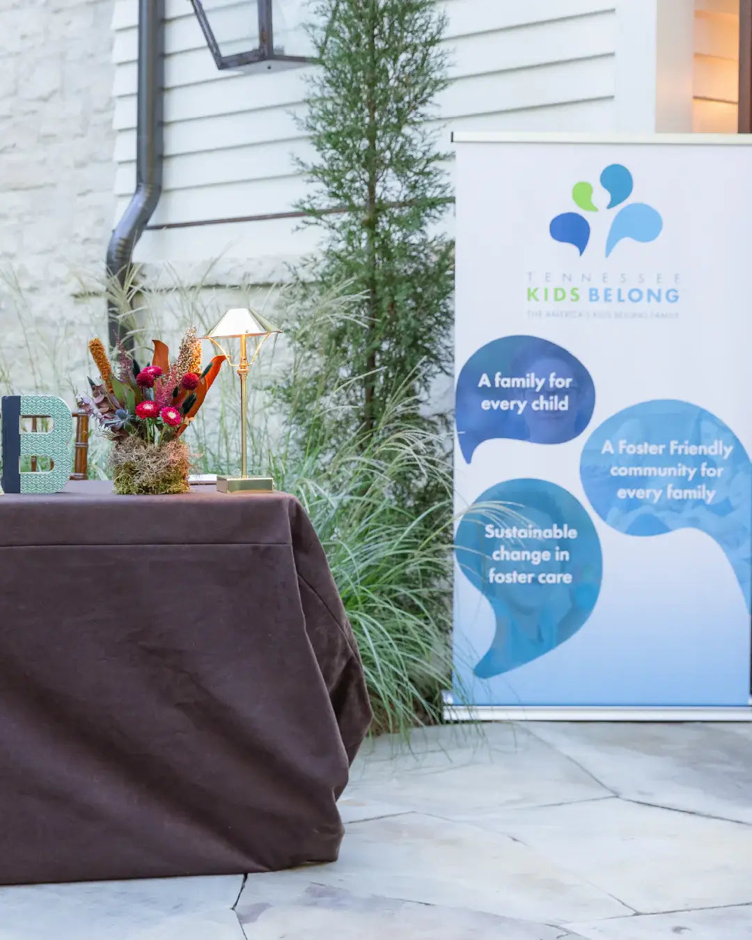 Table with decorative items next to a 'Foster Kids Belong' sign outdoors.