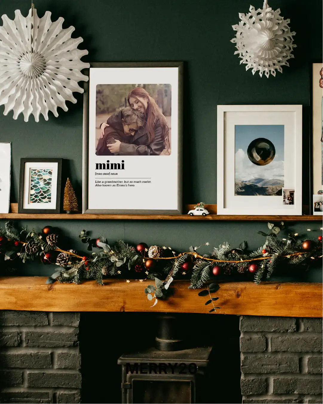 Decorative mantel with framed pictures, a garland, and wall art against a dark green wall.