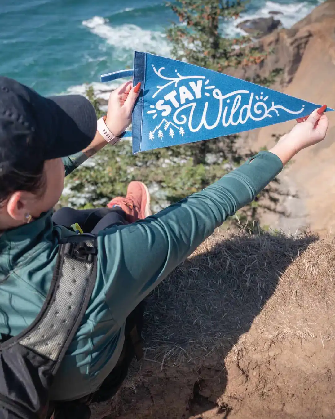 Person holding a blue 'Stay Wild' pennant by the ocean